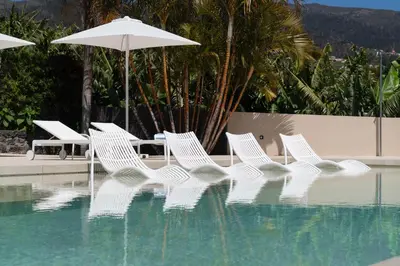 a group of white chairs and an umbrella next to a pool at OurMadeira - Bellissima in Estreito da Calheta