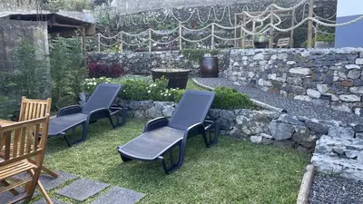 a group of chairs sitting in a yard with a stone wall at Casas das Hortas, Apartamento Vista Mar in Seixal