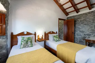 a bedroom with two beds and a stone wall at Villa Roque by An Island Apart in Calheta