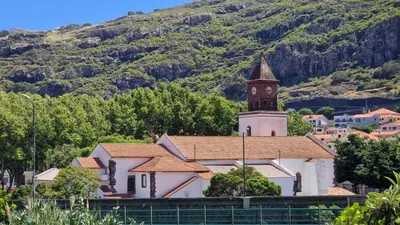 a church with a clock tower in front of a mountain at Casa D'Além I & II by LovelyStay in Machico