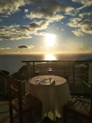 a table with wine glasses on a balcony with the sunset at Casa Menezes Sunrise and Sunset Every Day in Calheta