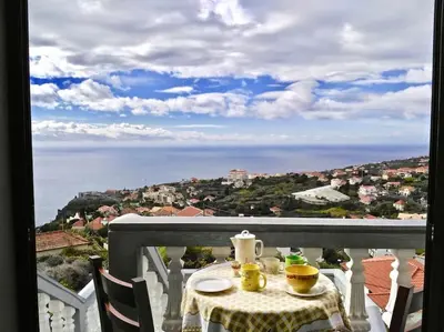 a table with two cups on a balcony with a view of the ocean at Casa Menezes Sunrise and Sunset Every Day in Calheta