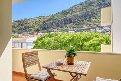 a table and chair on a balcony with a mountain at Machico Fachos View, a Home in Madeira in Machico