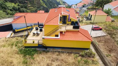 a yellow house with an orange roof on a hill at Casinha Gomes in Calheta
