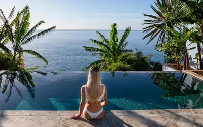 a woman sitting on the edge of a pool looking out at the ocean at Pirate House Sea front Private Pool Garden Funchal in Funchal