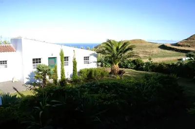a white house with palm trees and a hill at Aldeia in Chã de João Tomé