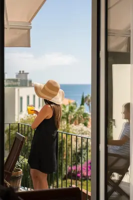 a woman in a hat standing on a balcony looking at the ocean at Bela de Santiago I by An Island Apart in Funchal