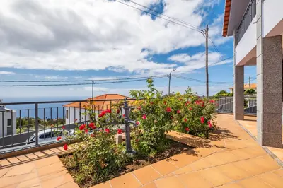 a balcony with red flowers and a building at Linda Paisagem in Calheta