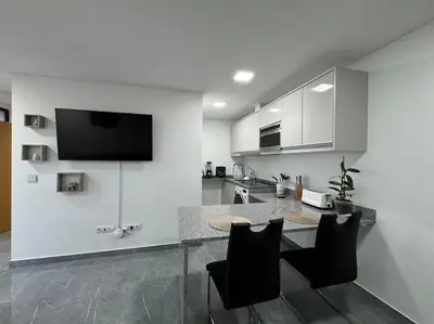 a white kitchen with a table and black chairs at Villa Castanho II in Calheta