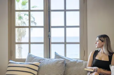 a woman sitting on a bed looking out a window at Hilani House by Homie in São Vicente