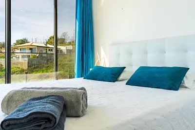 a large bed with blue pillows and a large window at Casa Branca-A, beautiful sea view in Estreito da Calheta