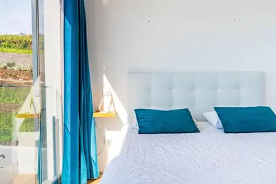 a bedroom with a bed with blue pillows and a window at Casa Branca-A, beautiful sea view in Estreito da Calheta