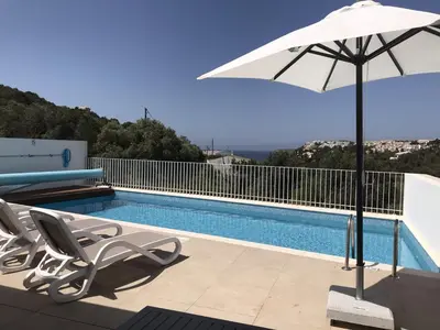 a swimming pool with a white umbrella and chairs and a pool at Casa Turquesa in Salema