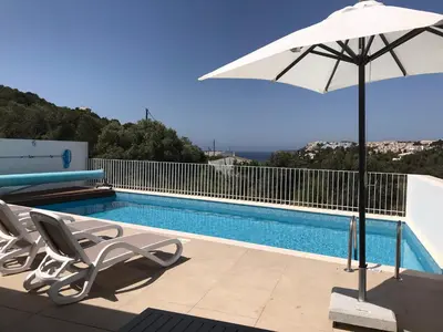 a swimming pool with a white umbrella and chairs and a pool at Casa Turquesa in Salema
