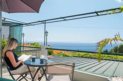 a woman sitting at a table on a balcony reading a book at Harmony Retreat by Homie in Ponta do Sol