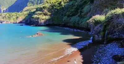 a beach with people walking on the sand and the water at Estúdio Costinha - Madeira in Garajau