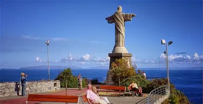 a statue of a christ redeemer with people sitting on benches at Estúdio Costinha - Madeira in Garajau