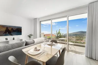 a living room with a table and chairs and a large window at Brand new apartment - Balcony with sea view in Arco da Calheta