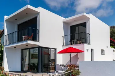 a white house with a red umbrella and a patio at Mouras House, Arco da Calheta in Arco da Calheta
