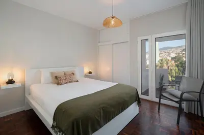 a white bedroom with a large bed and a chair at Apartamento Jaime Moniz by An Island Apart in Funchal