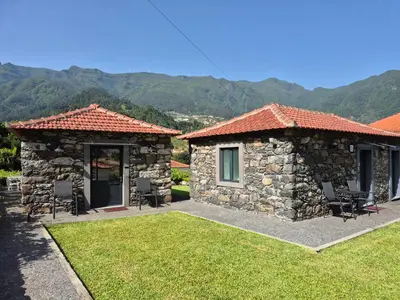a stone house with a patio with chairs and mountains at Casa da Vicencia in São Vicente