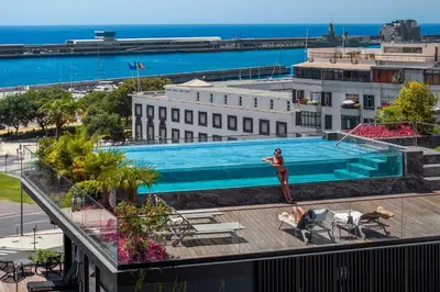 a woman standing next to a swimming pool on top of a building at Savoy Insular Loft by An Island Apart in Funchal