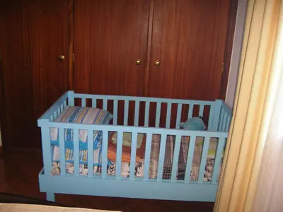 a white crib in a room with wooden cabinets at Residencia ANA Piso Um 1 in Santa Cruz