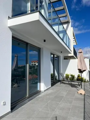 a white house with glass doors and a balcony at Holiday House Caetano in Ponta do Sol