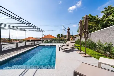 a swimming pool with umbrellas next to a house at Luxury Retreat in Camara de Lobos in Câmara de Lobos