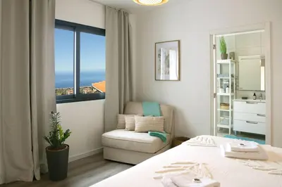 a bedroom with a bed and a chair and a window at Vila Rouxinol in Arco da Calheta