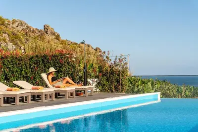 a woman sitting in a chair next to a swimming pool at Oak Tree Ocean View in Ponta do Sol
