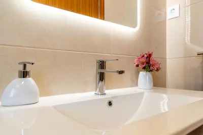 a bathroom sink with a mirror and a vase of flowers at Goncalves House - AC and private parking in Calheta