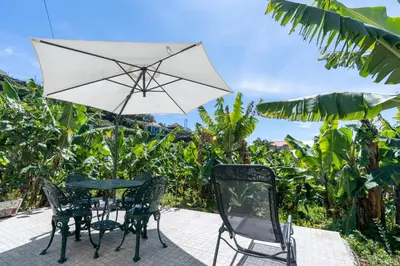 a table and two chairs and an umbrella at Sleep Among the Bananas! Rustic Cottage with Trails at Your Doorstep in Ponta do Sol