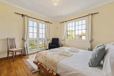 a bedroom with a bed and a chair and two windows at Palm Tree House by Homie in Ponta Delgada