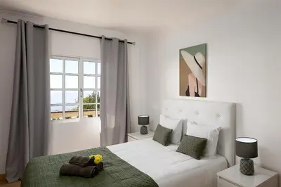 a white bedroom with a bed and a window at Franco's House, mar e serra in Estreito da Calheta