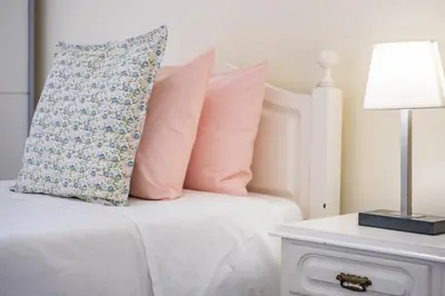a white bed with pink pillows and a table with a lamp at Cantinho dos Ilhéus in Funchal