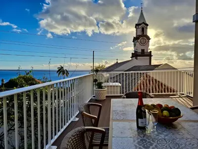 a table with a bowl of fruit on a balcony with a clock tower at Casa Neves in Arco da Calheta