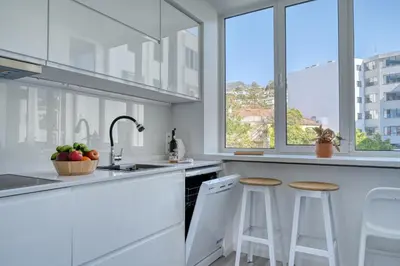a white kitchen with a sink and two bar stools at Maranta House, a Home in Madeira in Funchal