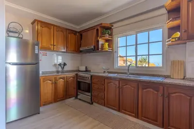 a kitchen with wooden cabinets and a stainless steel refrigerator at Alegria Apart. with Pool, by Pausa Holiday Rentals in Estreito da Calheta
