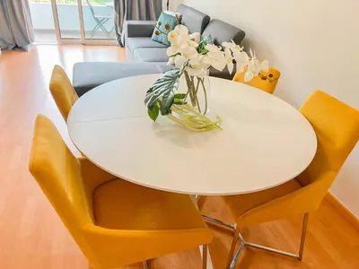 a white dining room table with yellow chairs and a vase of flowers at Sandie's Serene Stay in Caniço