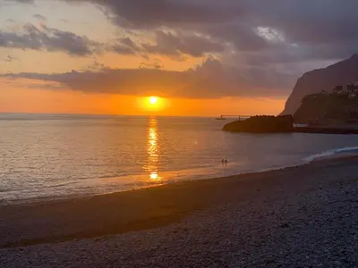 a sunset on a beach with a person in the water at Pakisa-Holidays in Funchal
