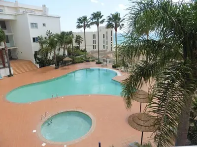 a large swimming pool with palm trees and a building at Superbe appartement vue mer et falaises in Lagos
