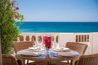 a table with glasses and a vase with flowers on it at Beachfront Apartment Praia da Luz by Blue Diamond 23B in Luz