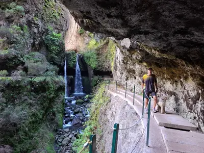 a man walking a dog on a path with a waterfall at Sallys in Ponta do Sol