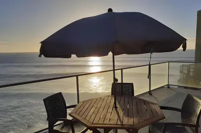 a table and chairs with an umbrella on a balcony at The Wave House - Seaside Haven in Jardim do Mar