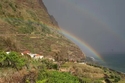 a rainbow over a village on a hill with the ocean at Original Wave House in Jardim do Mar