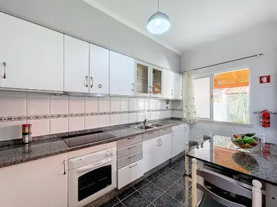 a kitchen with white cabinets and a sink and a table at Eddys House by Atlantic Holiday in Água de Pena