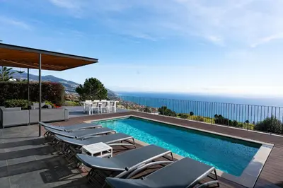 a swimming pool with chairs and a view of the ocean at Villa Eden Nature in Prazeres in Prazeres