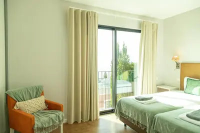 a bedroom with a bed and a chair and a window at Villa Eden Nature in Prazeres in Prazeres
