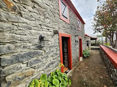 a stone building with a red door and some plants at Refugio Jardim Prazeres WiFi BBQ in Prazeres
